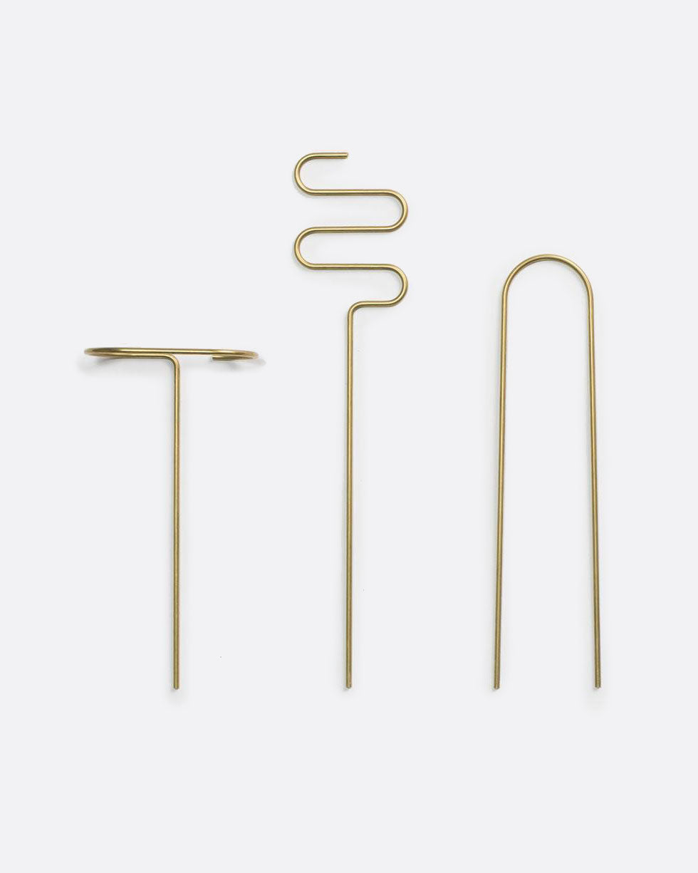 three brass plant sticks side by side on a white background, each one is bent into a different shape