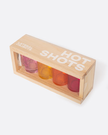 Four glass shot glasses in shades of pink, orange, and yellow, shown in their wood carrying case from the top.