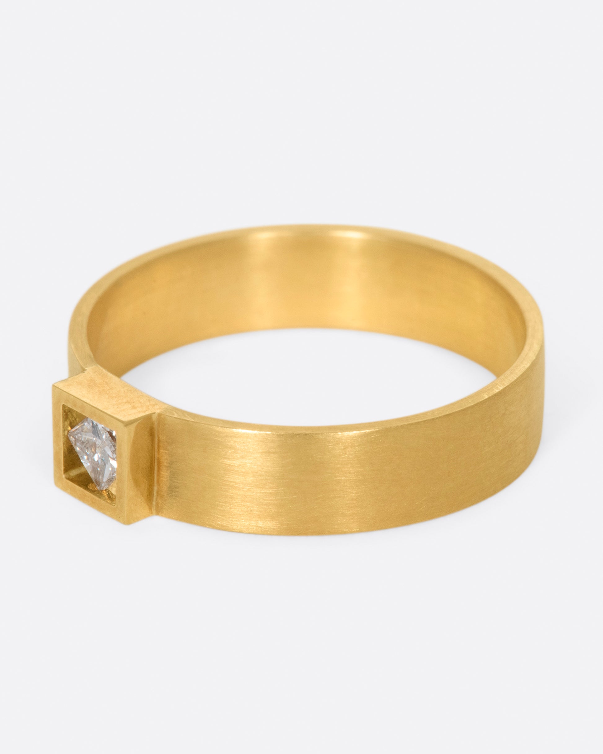 A wide, matte band ring with a princess cut diamond set at its center.