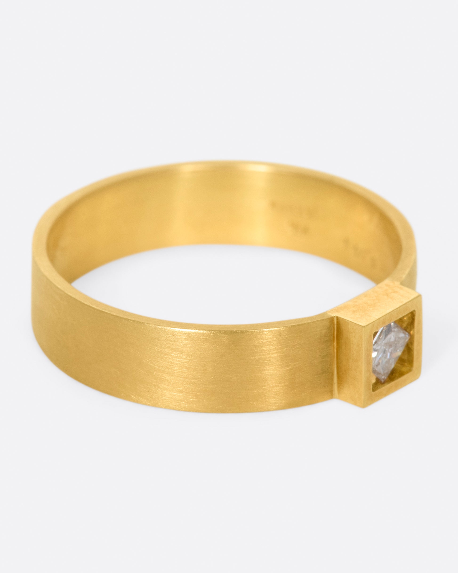 A wide, matte band ring with a princess cut diamond set at its center.