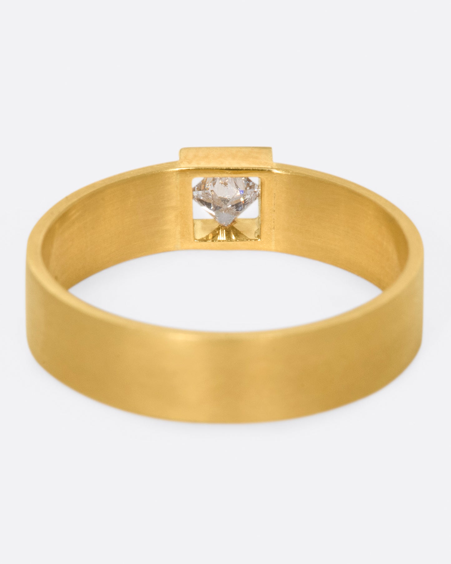 A wide, matte band ring with a princess cut diamond set at its center.