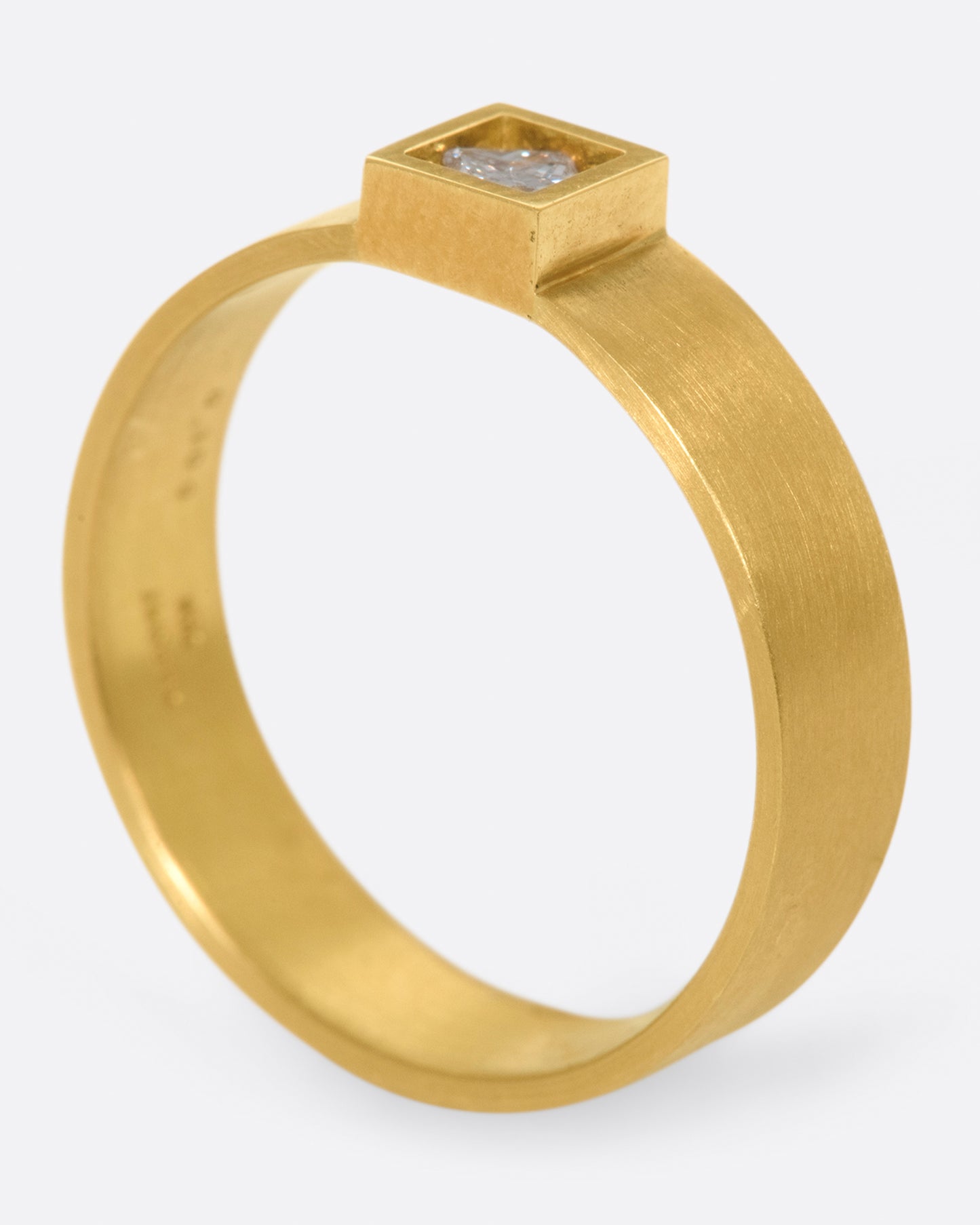 A wide, matte band ring with a princess cut diamond set at its center.