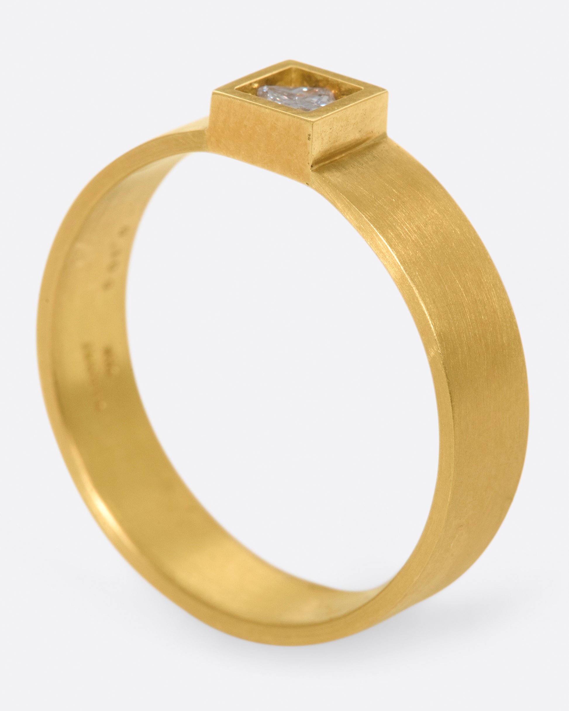 A wide, matte band ring with a princess cut diamond set at its center.