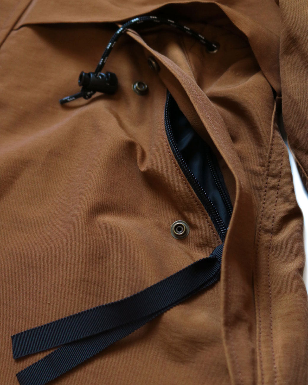 A close up of the zip and snap pocket on a brown parka with black toggles. 