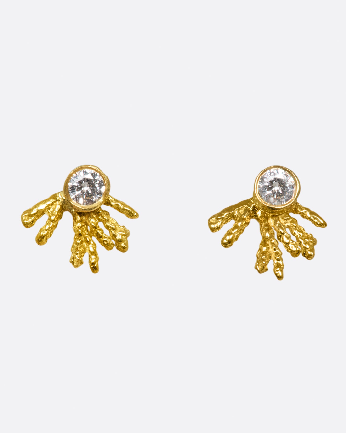 A pair of bezel set diamond studs with asymmetrical gold trails streaming behind them.