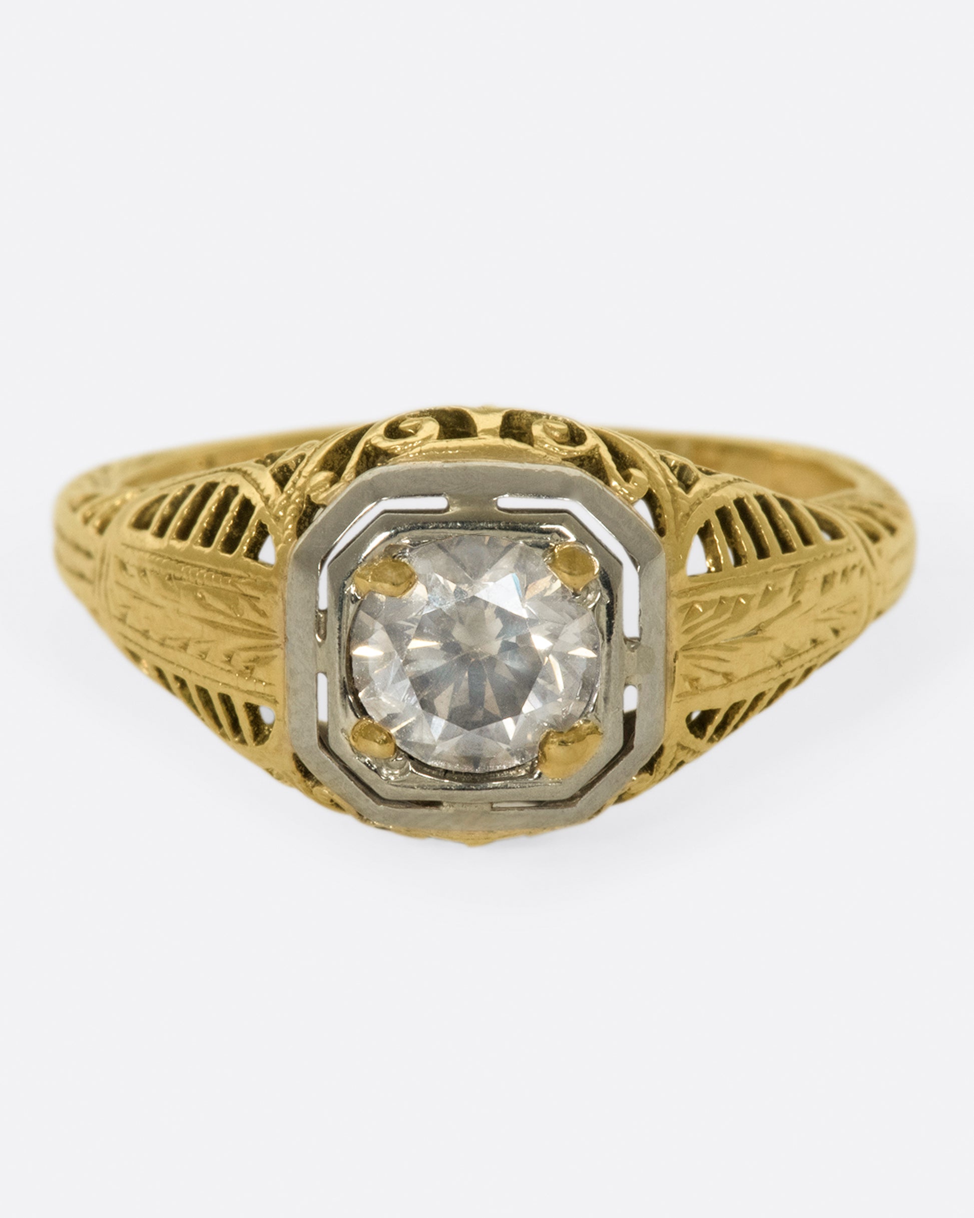 A filigree-covered signet ring with a champagne diamond at its center, set in a white gold bezel.