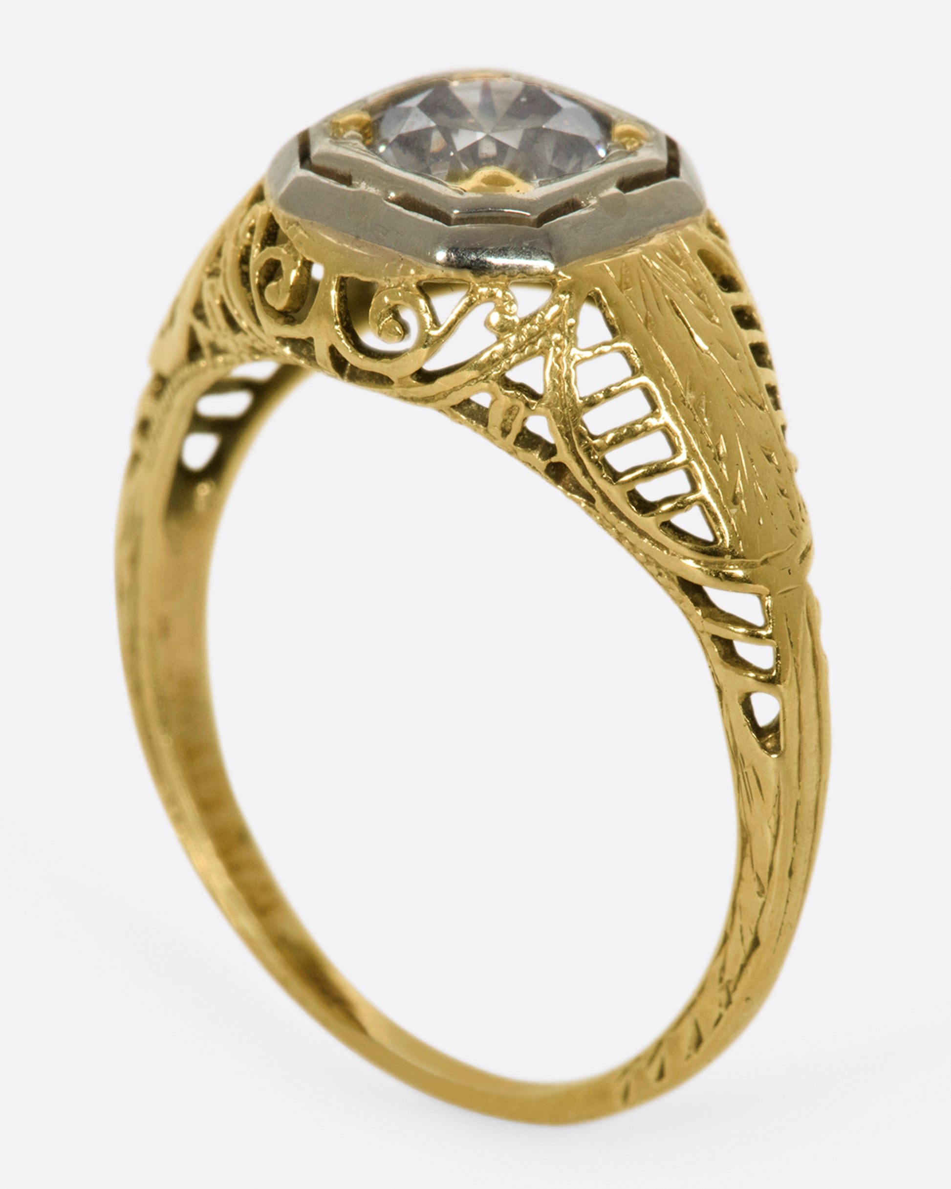 A filigree-covered signet ring with a champagne diamond at its center, set in a white gold bezel.