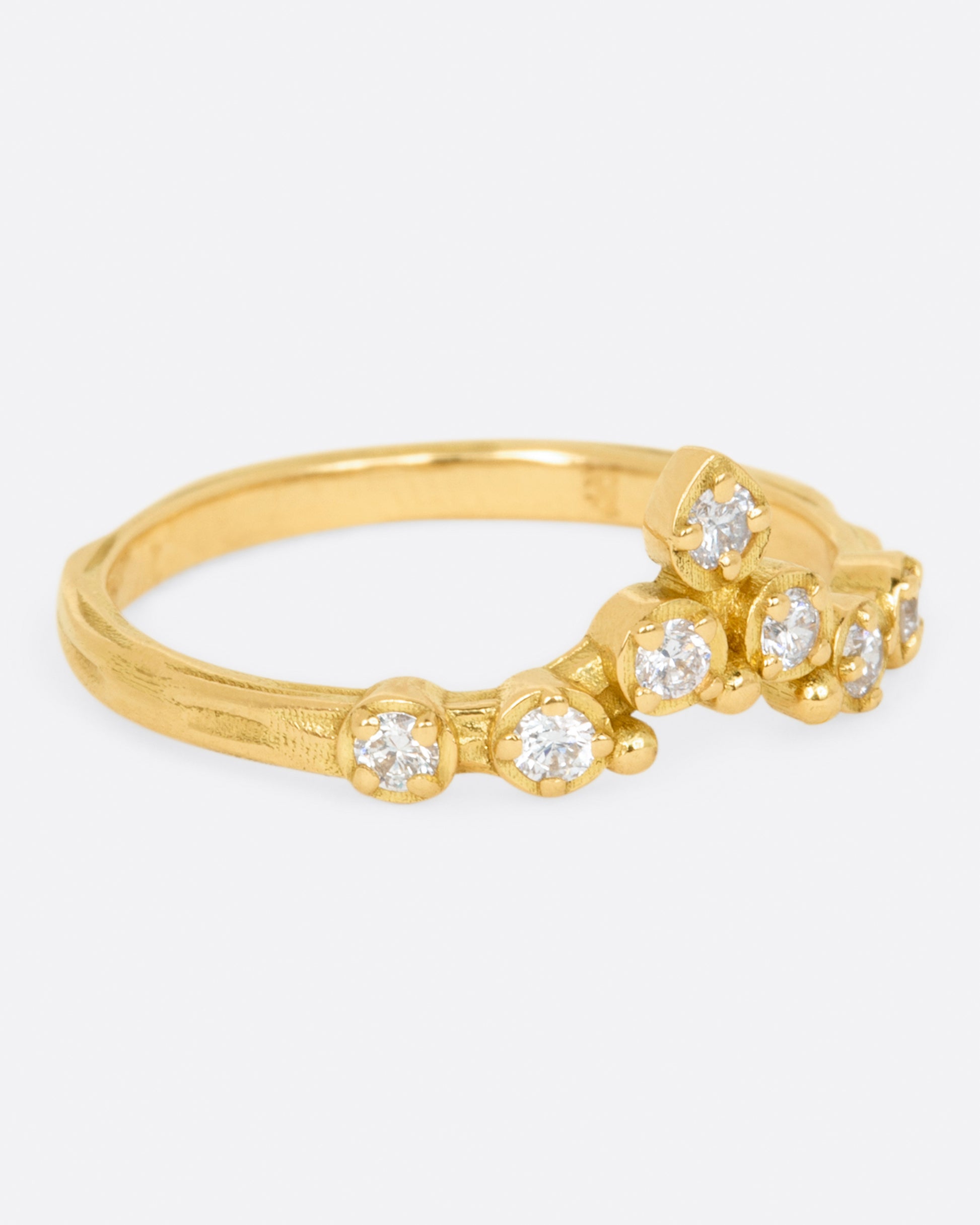 A slightly curved and pointed ring with seven diamonds on a textured band.