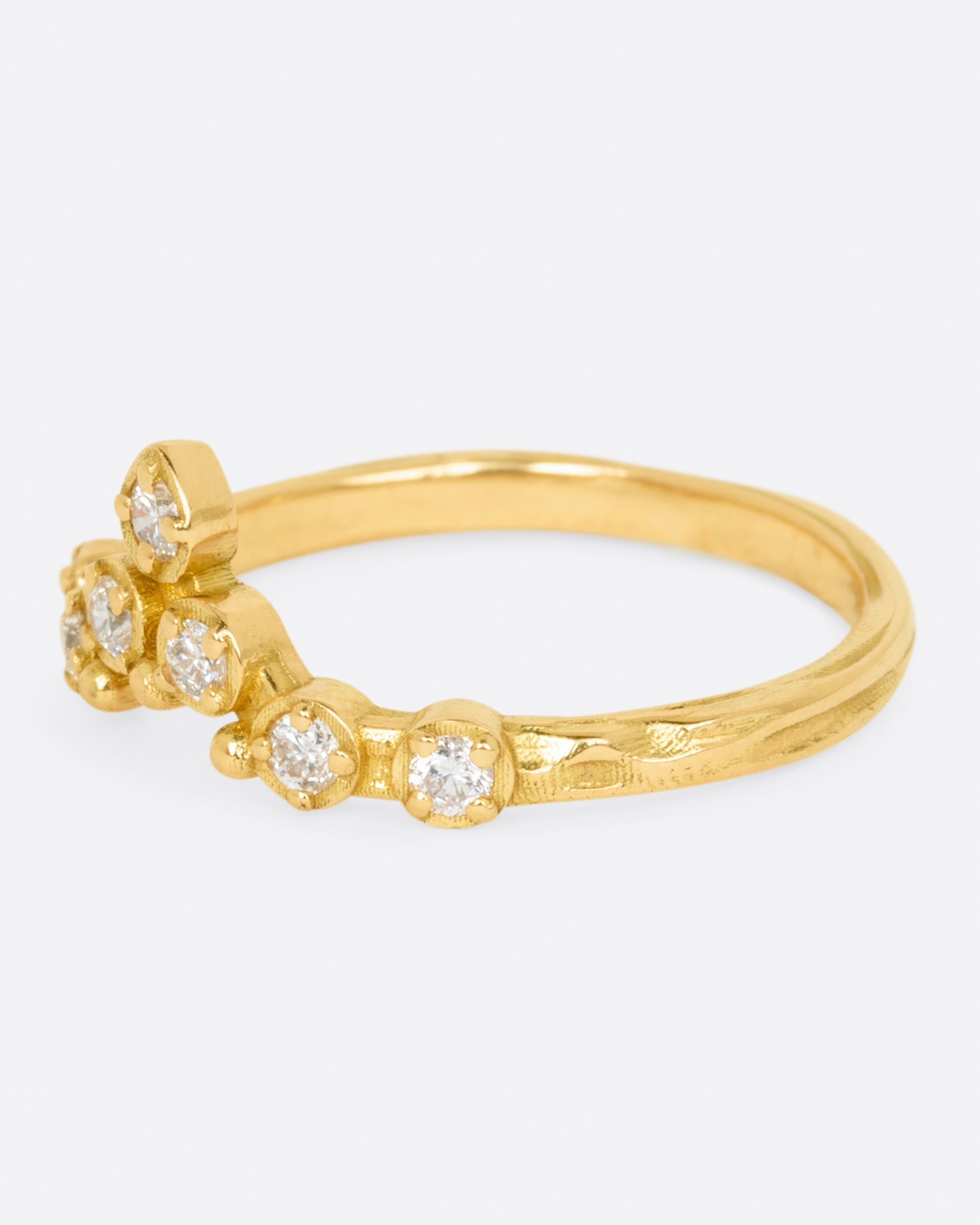 A slightly curved and pointed ring with seven diamonds on a textured band.