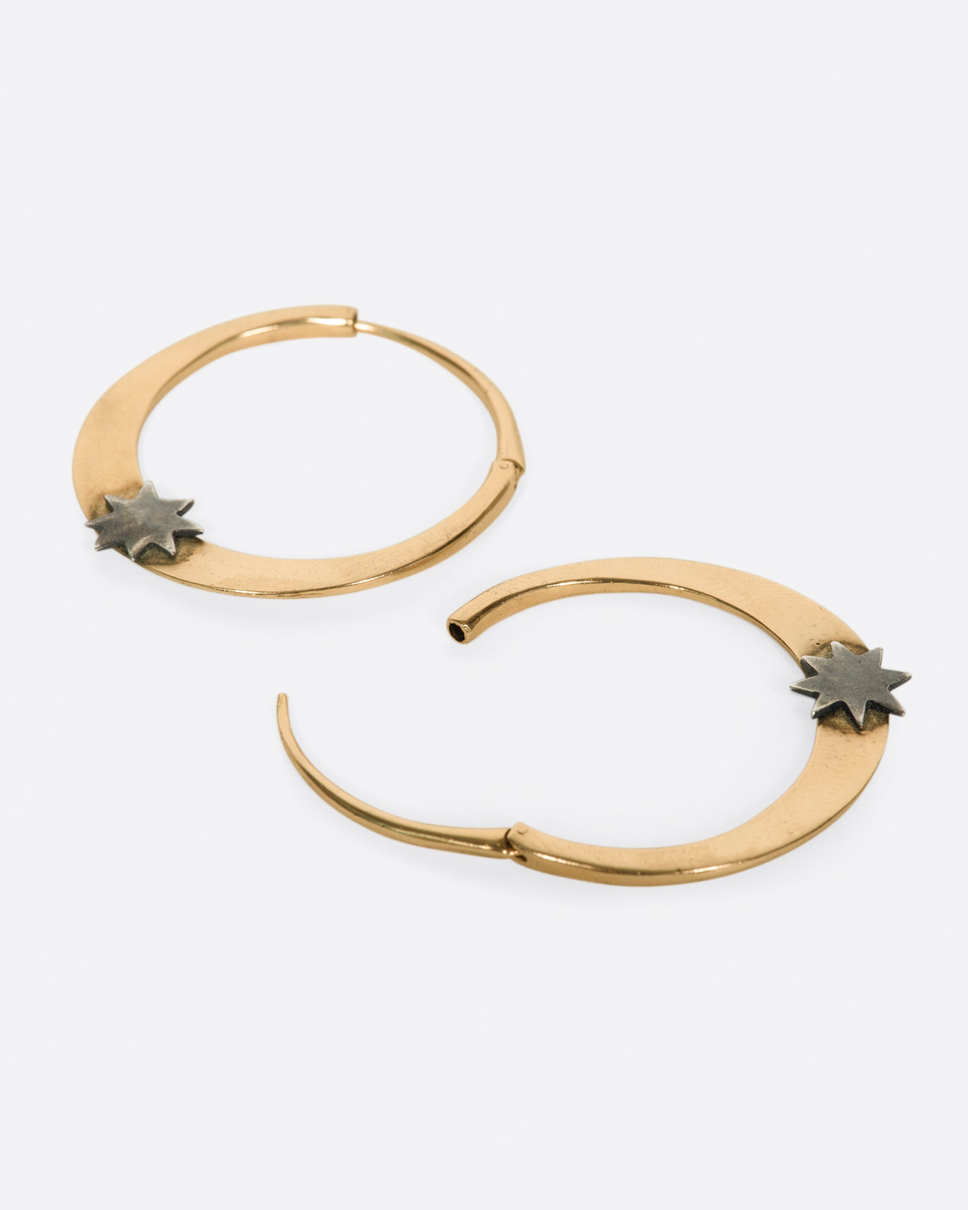 A pair of rose gold tapered hoop earrings with sterling silver stars at their base, shown laying flat.