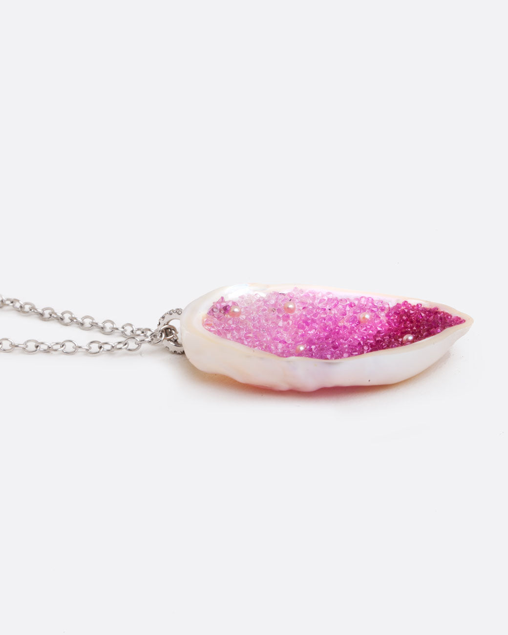 Close up side view of a large freshwater souffle pearl carved out and lined with ombre pink sapphires on a pendant with seed pearl accents and a pave diamonds on the bail.