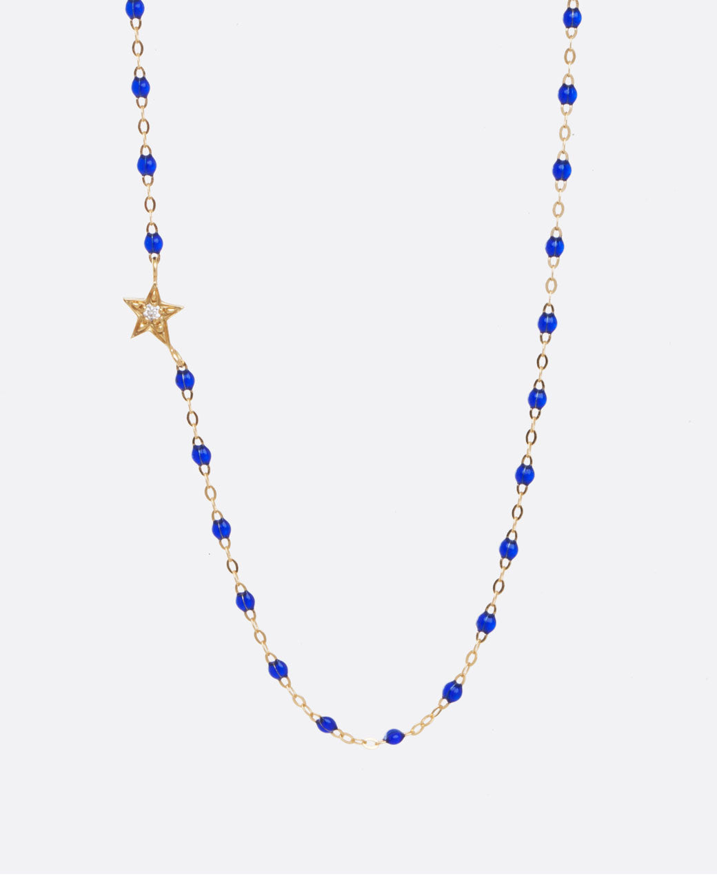 Yellow gold chain necklace with dark blue resin beads and off centered yellow gold star with diamond center