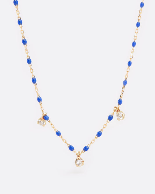 Close up birds eye view of yellow gold chain necklace with small blue resin beads with three diamond pendants alternating every two beads from the bottom of the necklace.