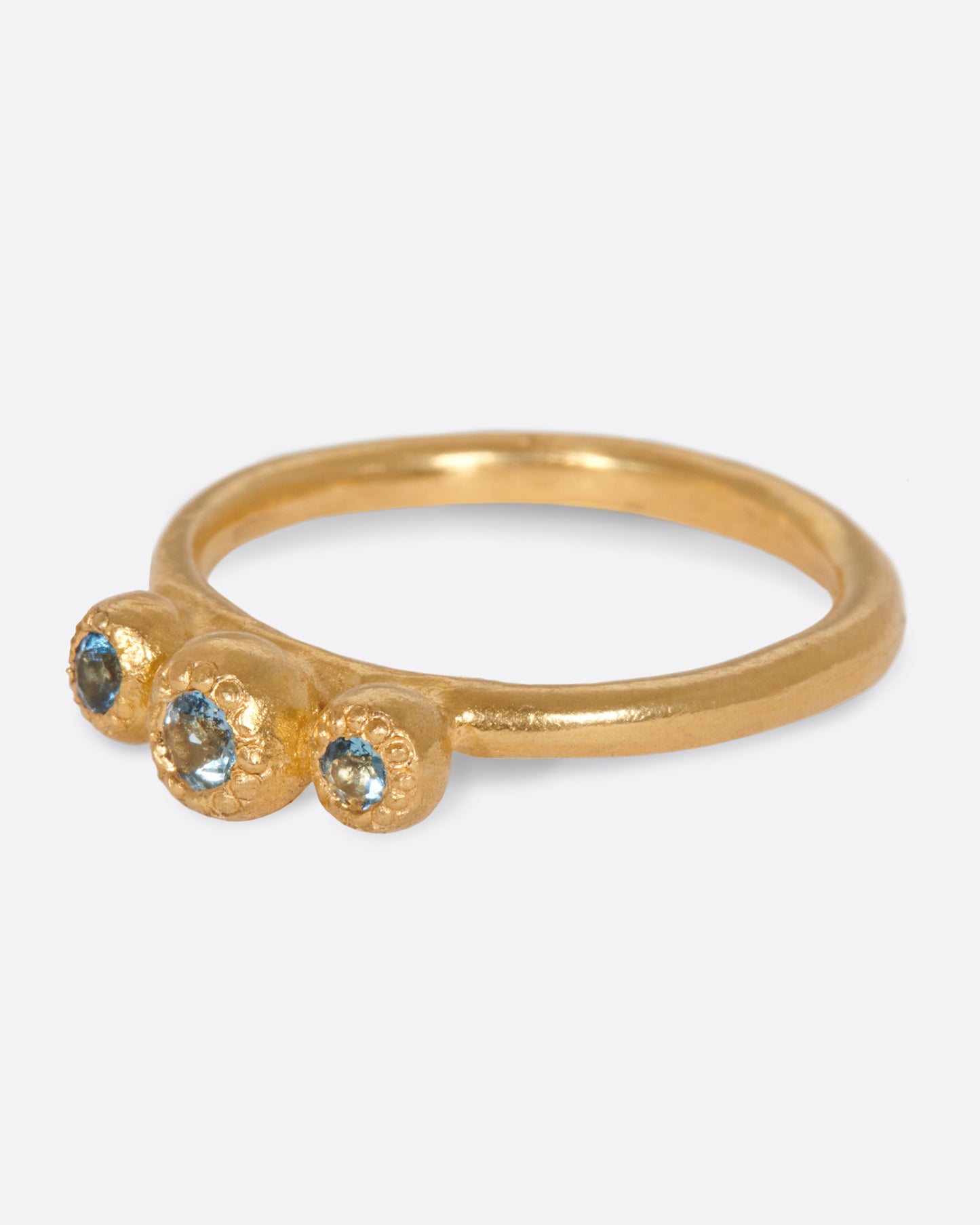 A handmade, high karat gold ring with three vibrant, bezel set aquamarines.