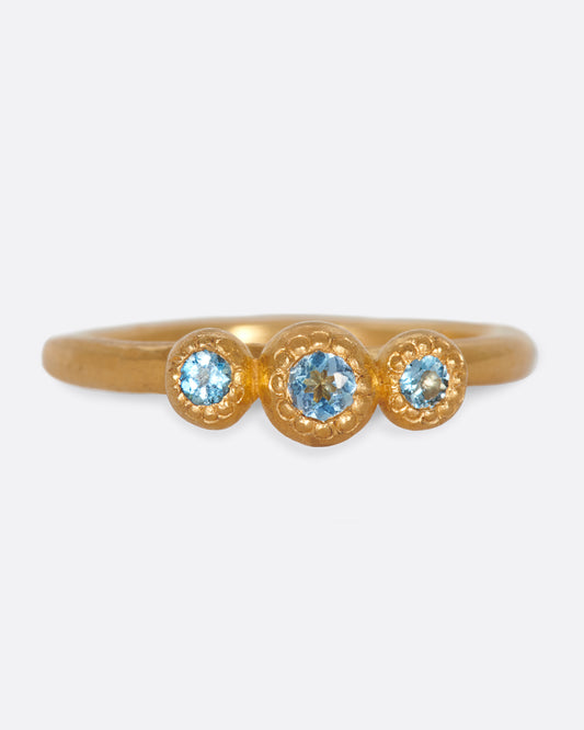 A handmade, high karat gold ring with three vibrant, bezel set aquamarines.