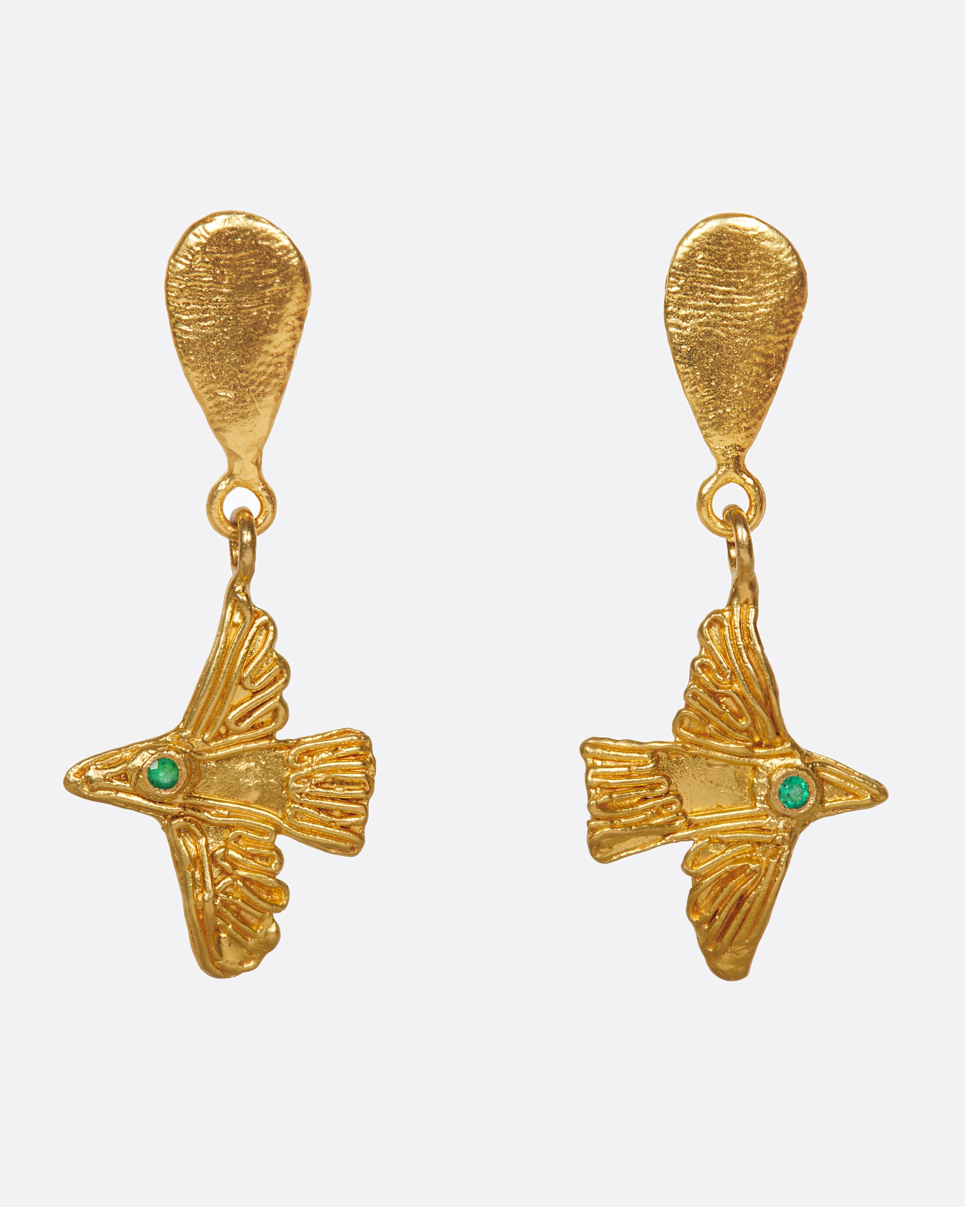 A pair of high karat gold drop earrings with flying birds and emerald eyes.