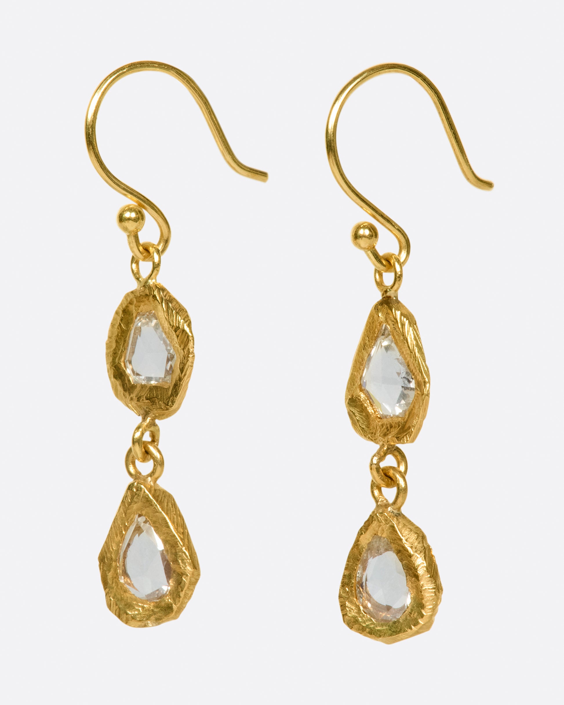 A pair of slightly asymmetrical diamond drop earrings with two diamonds set in hand carved bezels on each earring.