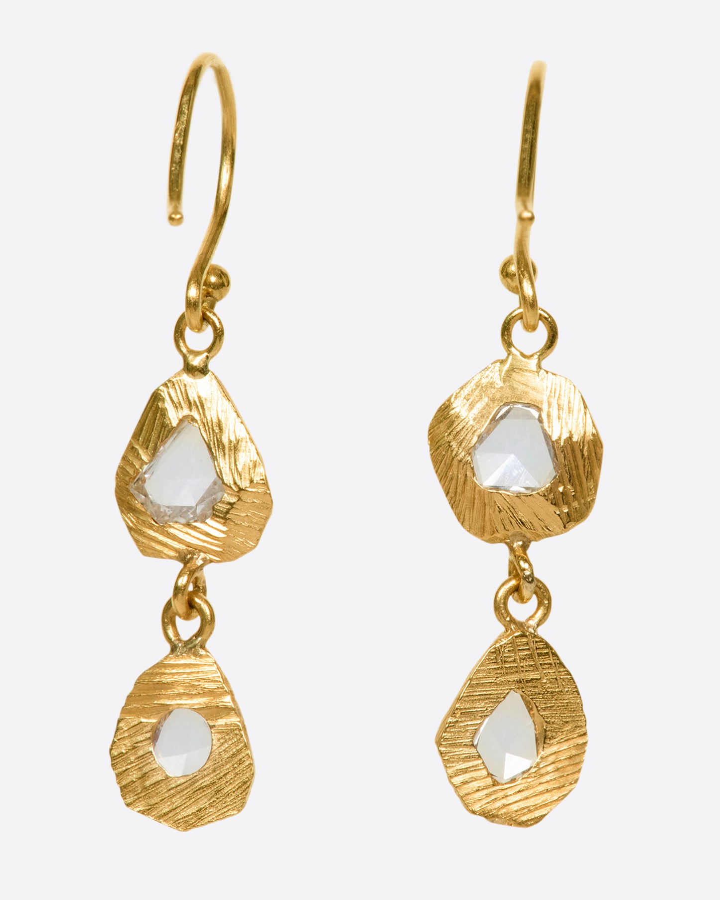 A pair of slightly asymmetrical diamond drop earrings with two diamonds set in hand carved bezels on each earring.