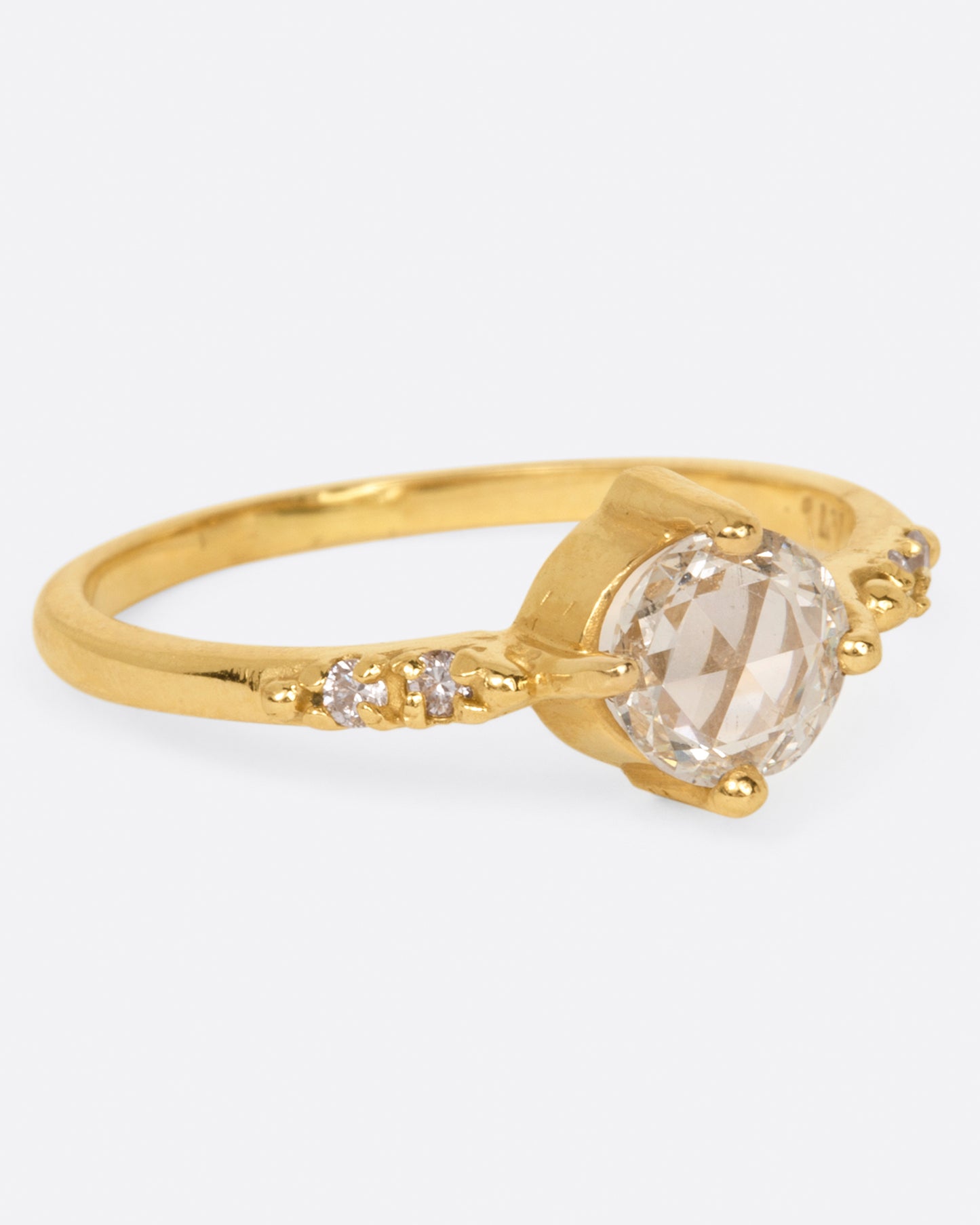 A yellow gold ring with a prong set rose cut diamond at the center and two diamonds on either side, shown from the side.