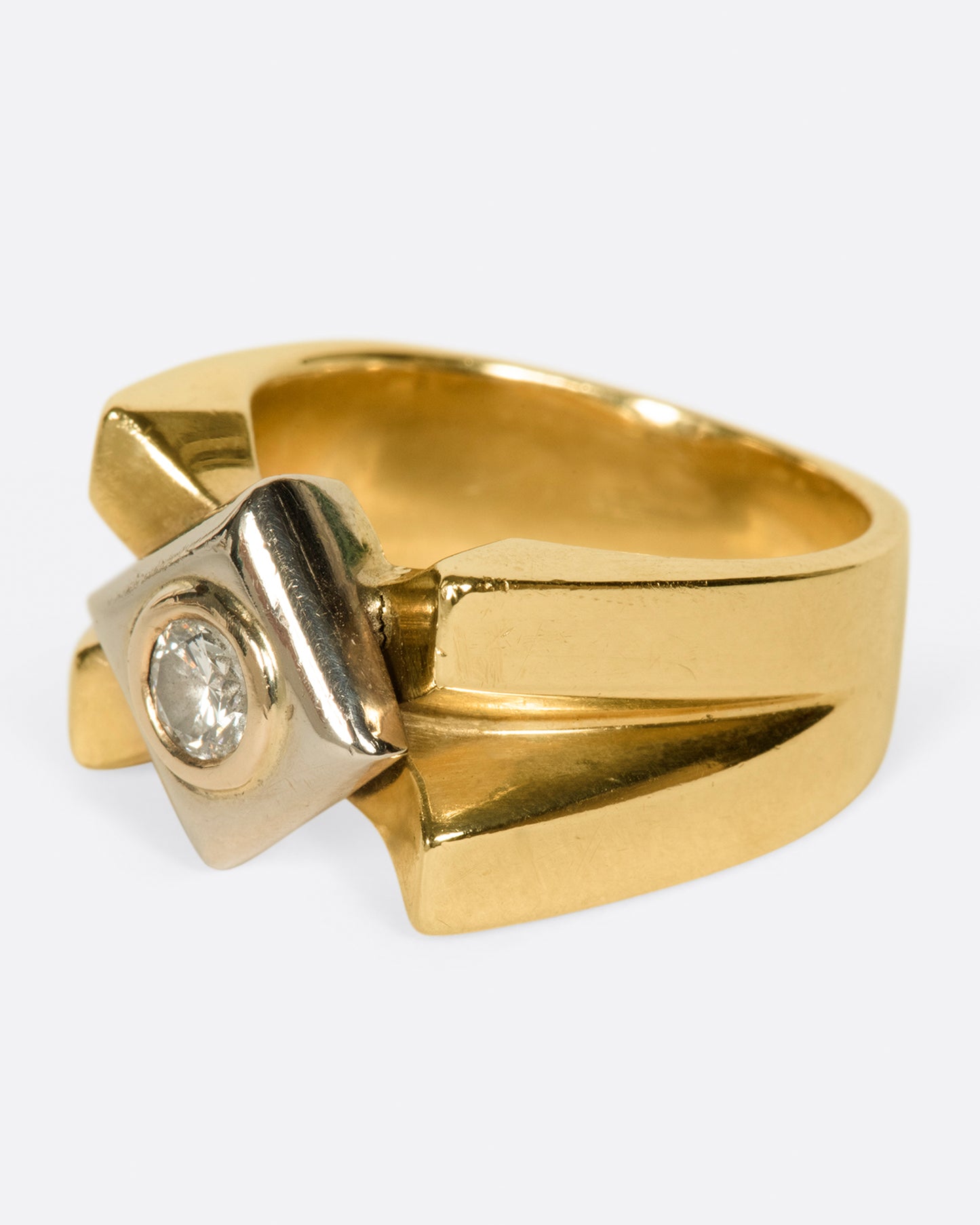 A heavy, gold, X-shaped ring with a white gold square and a round diamond at its center.