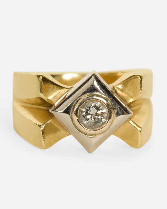 A heavy, gold, X-shaped ring with a white gold square and a round diamond at its center.