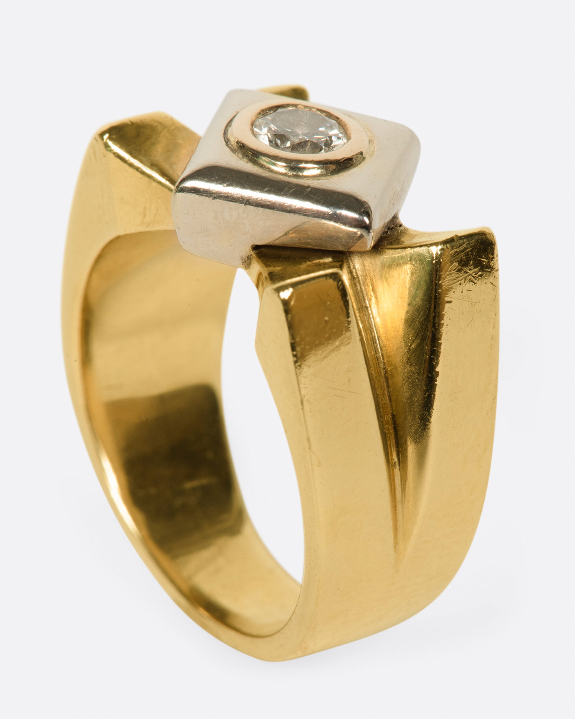 A heavy, gold, X-shaped ring with a white gold square and a round diamond at its center.