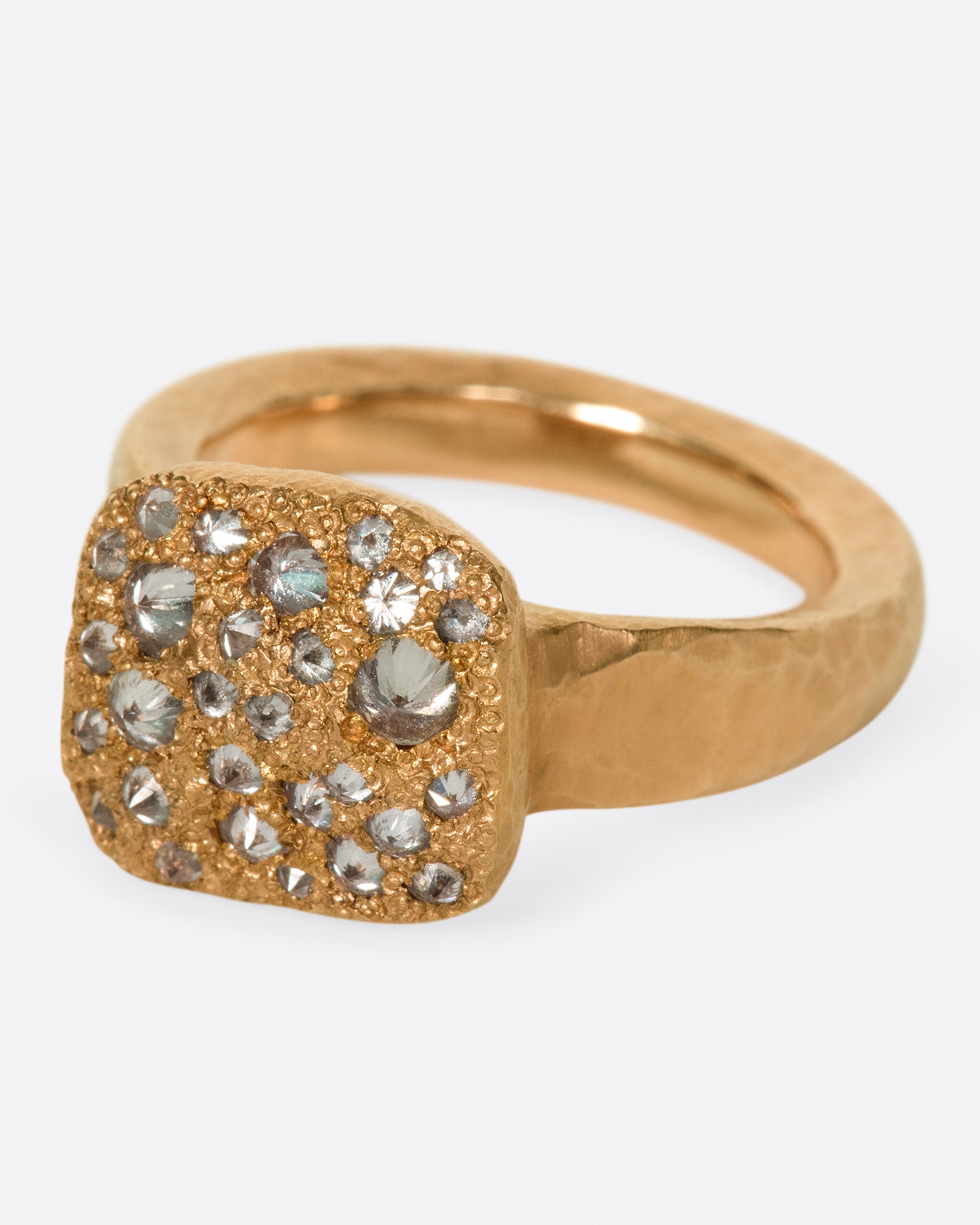 A hammered, hefty rose gold ring with inverted diamonds scattered across its rectangular face.