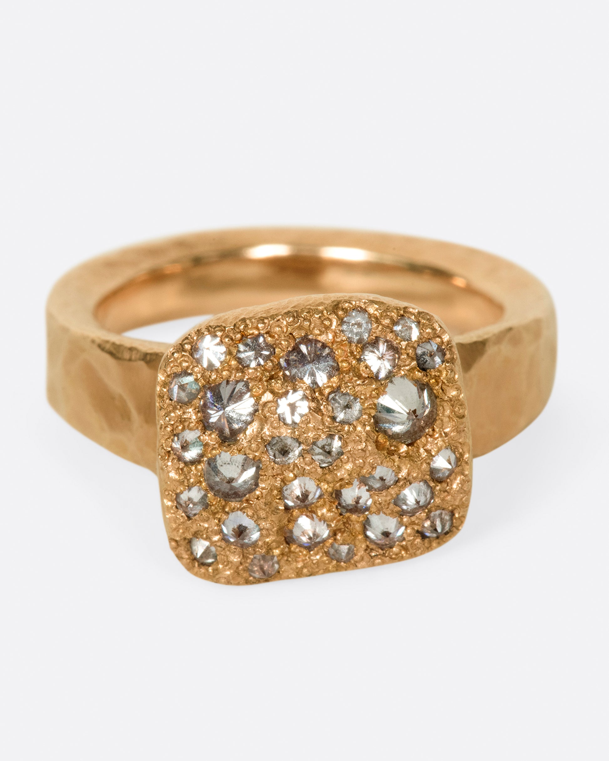 A hammered, hefty rose gold ring with inverted diamonds scattered across its rectangular face.