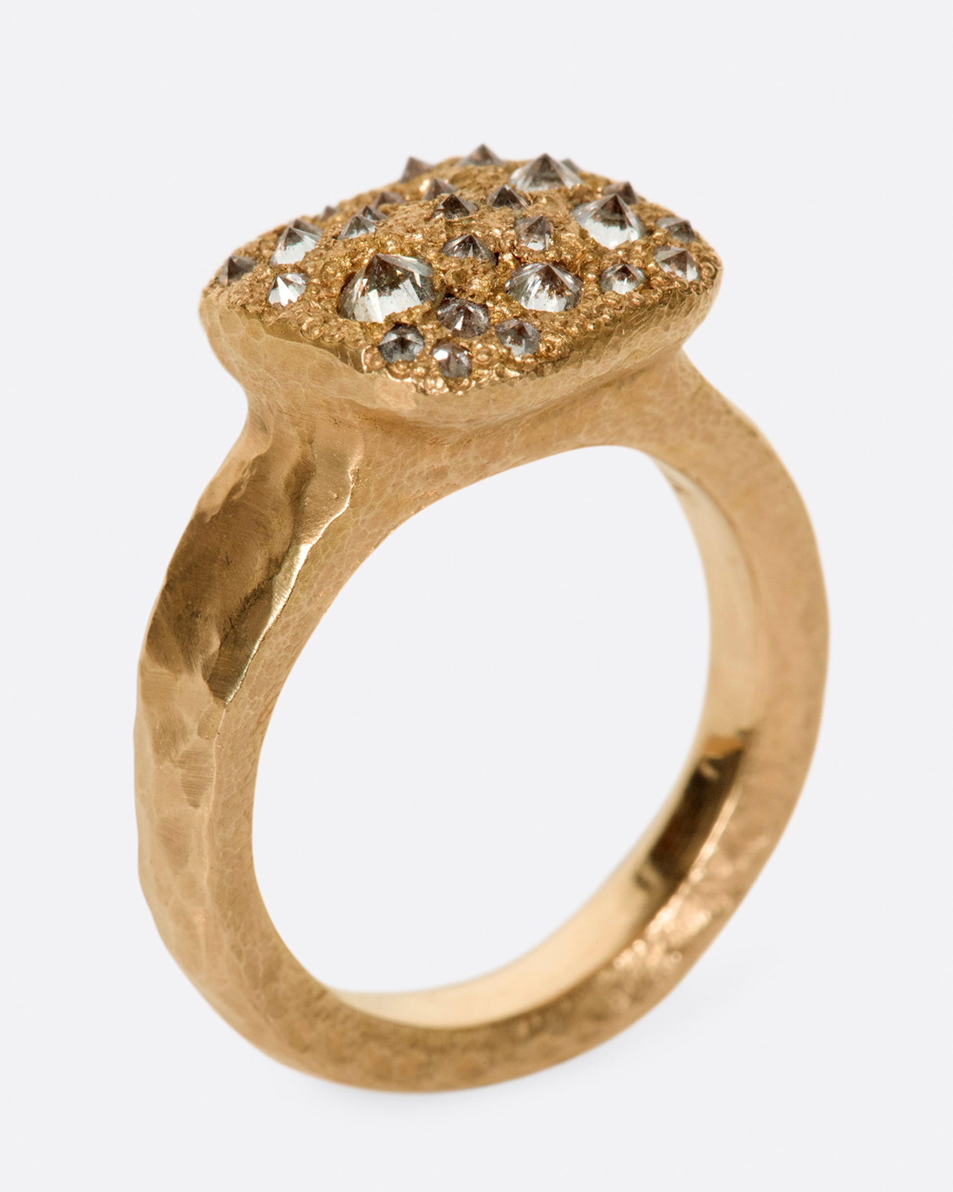 A hammered, hefty rose gold ring with inverted diamonds scattered across its rectangular face.