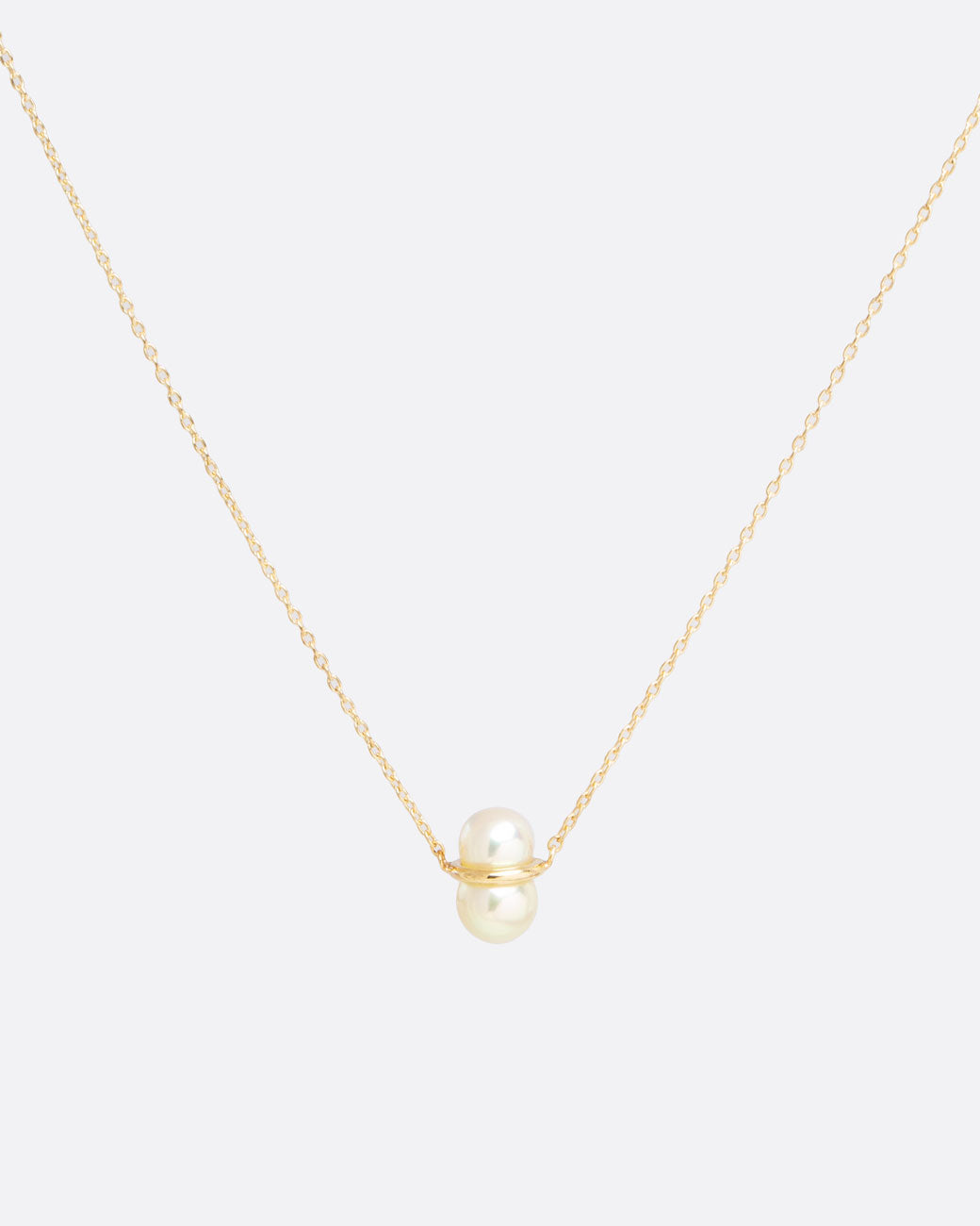 two pearls sit vertically stacked and connected by a gold setting. attached to a thin gold chain to make into a necklace.