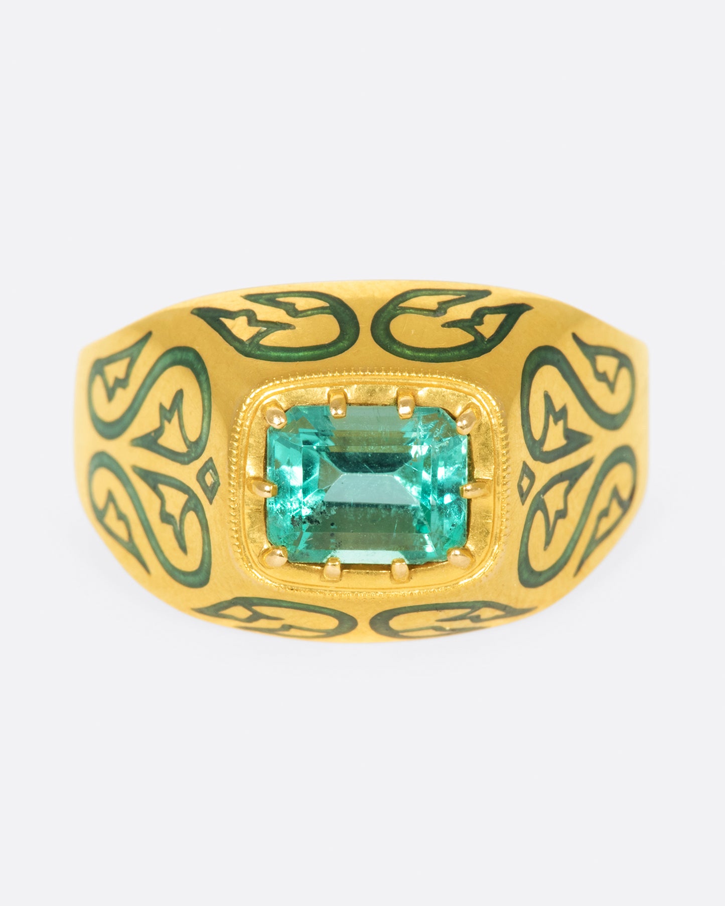 A gold ring featuring a bright Colombian emerald at its center and matching enamel details.