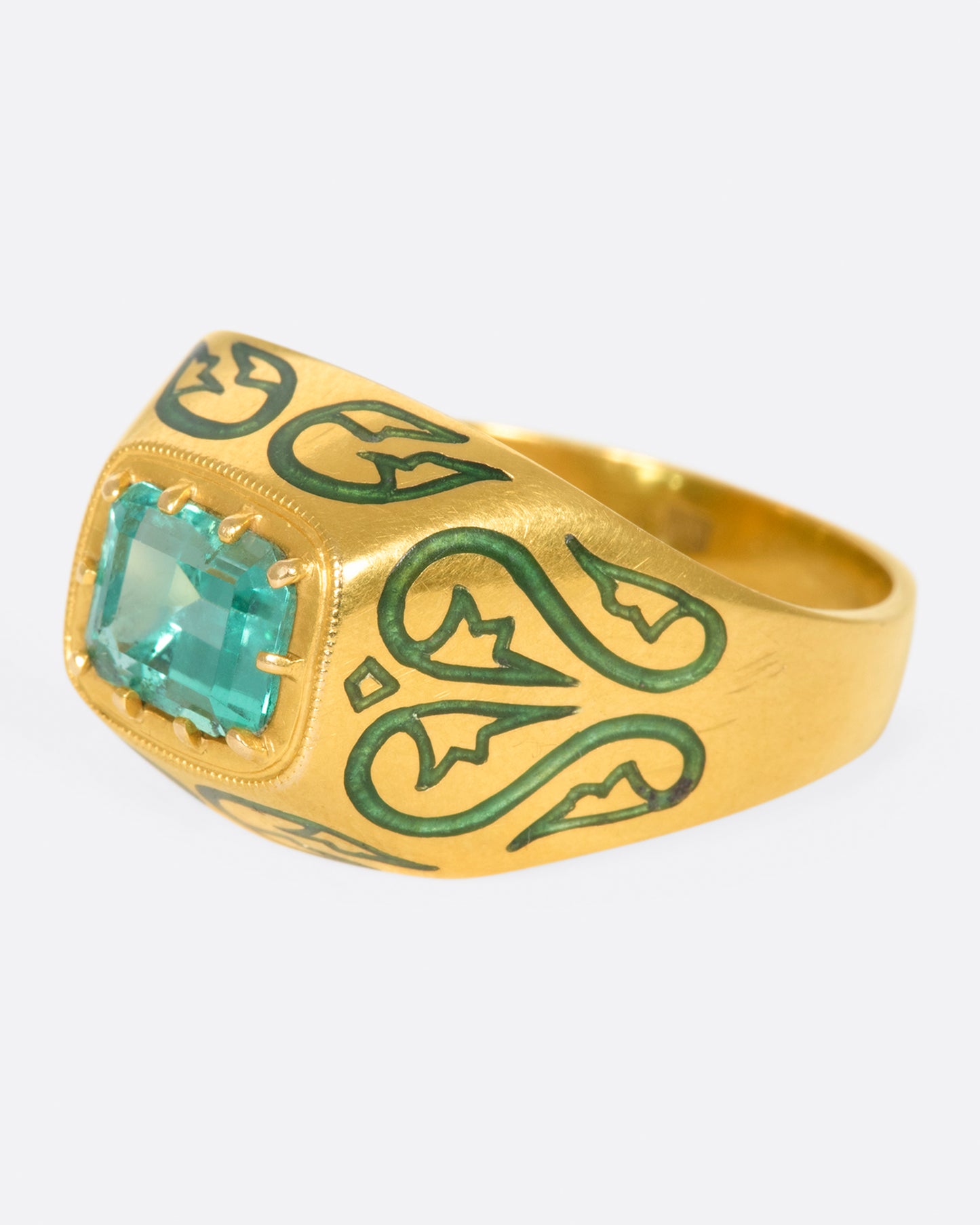 A gold ring featuring a bright Colombian emerald at its center and matching enamel details.