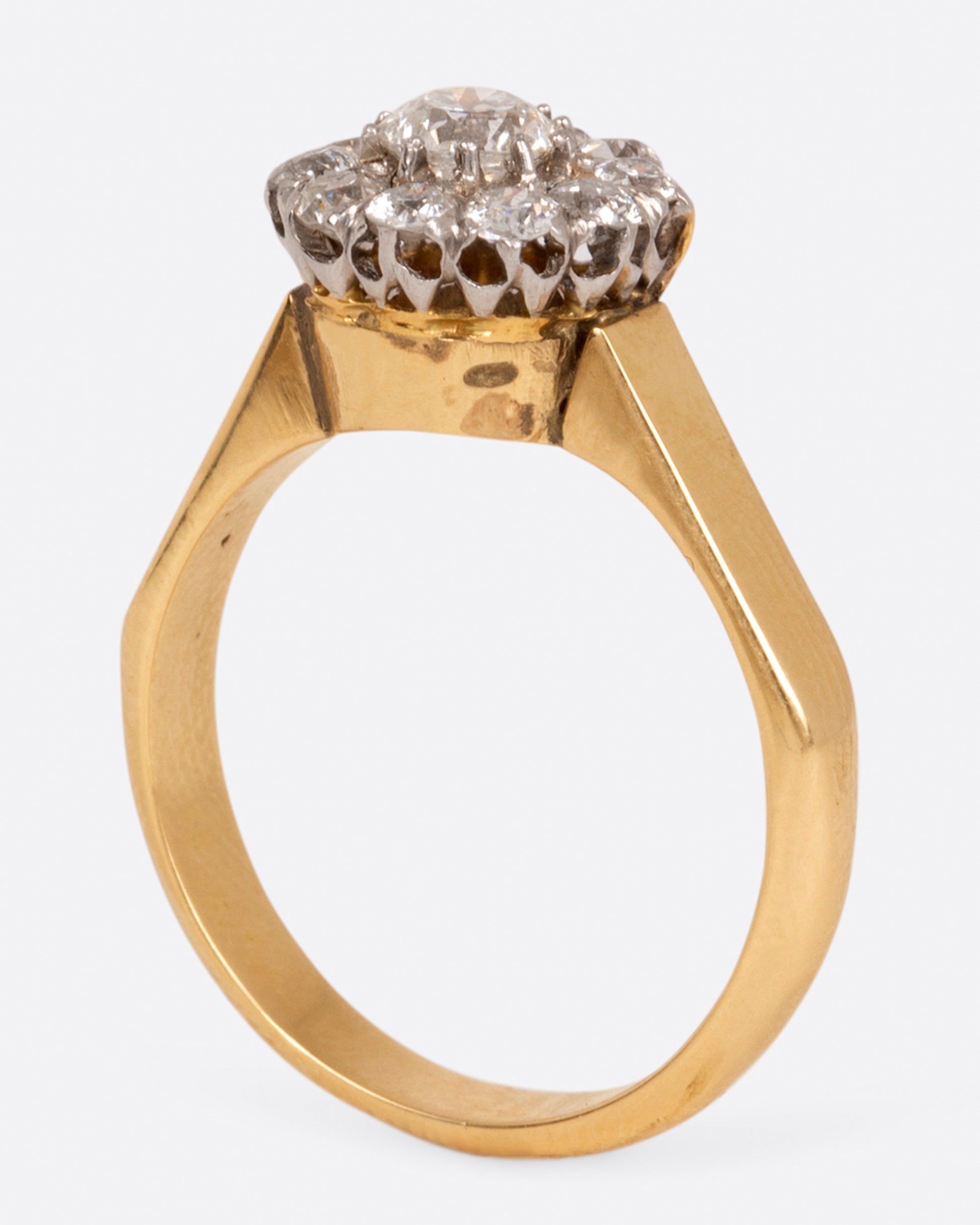 A wide flat yellow gold ring with a flower-shaped cluster of diamonds, shown standing.