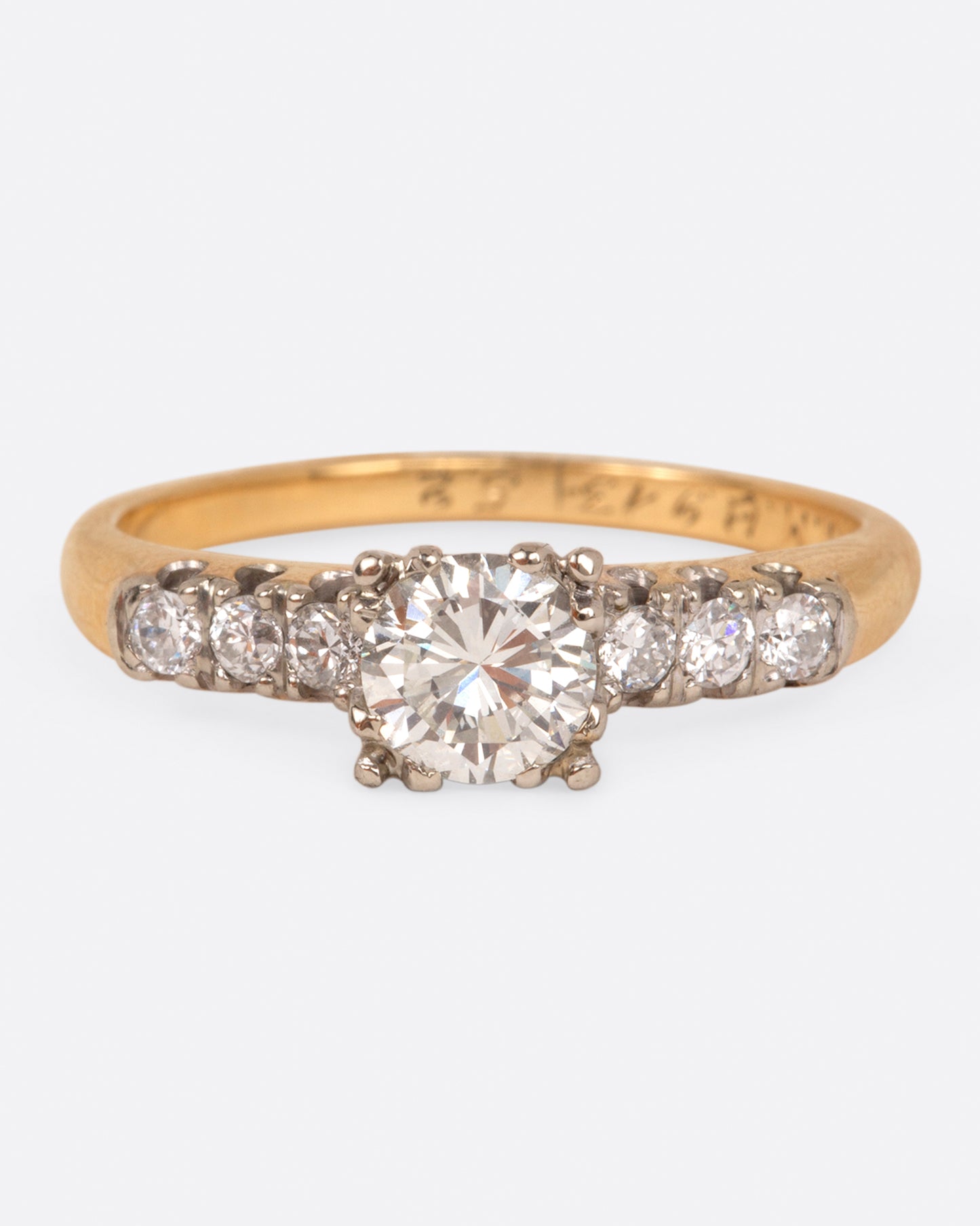 A yellow gold ring with a round center diamond and three smaller round diamonds on either side set in white gold prongs, shown from the front.