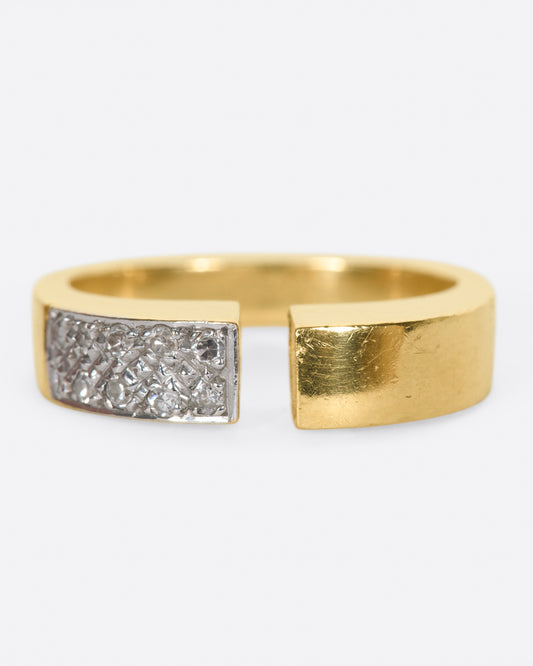 A raised, open, yellow gold ring with one pavé diamond corner.