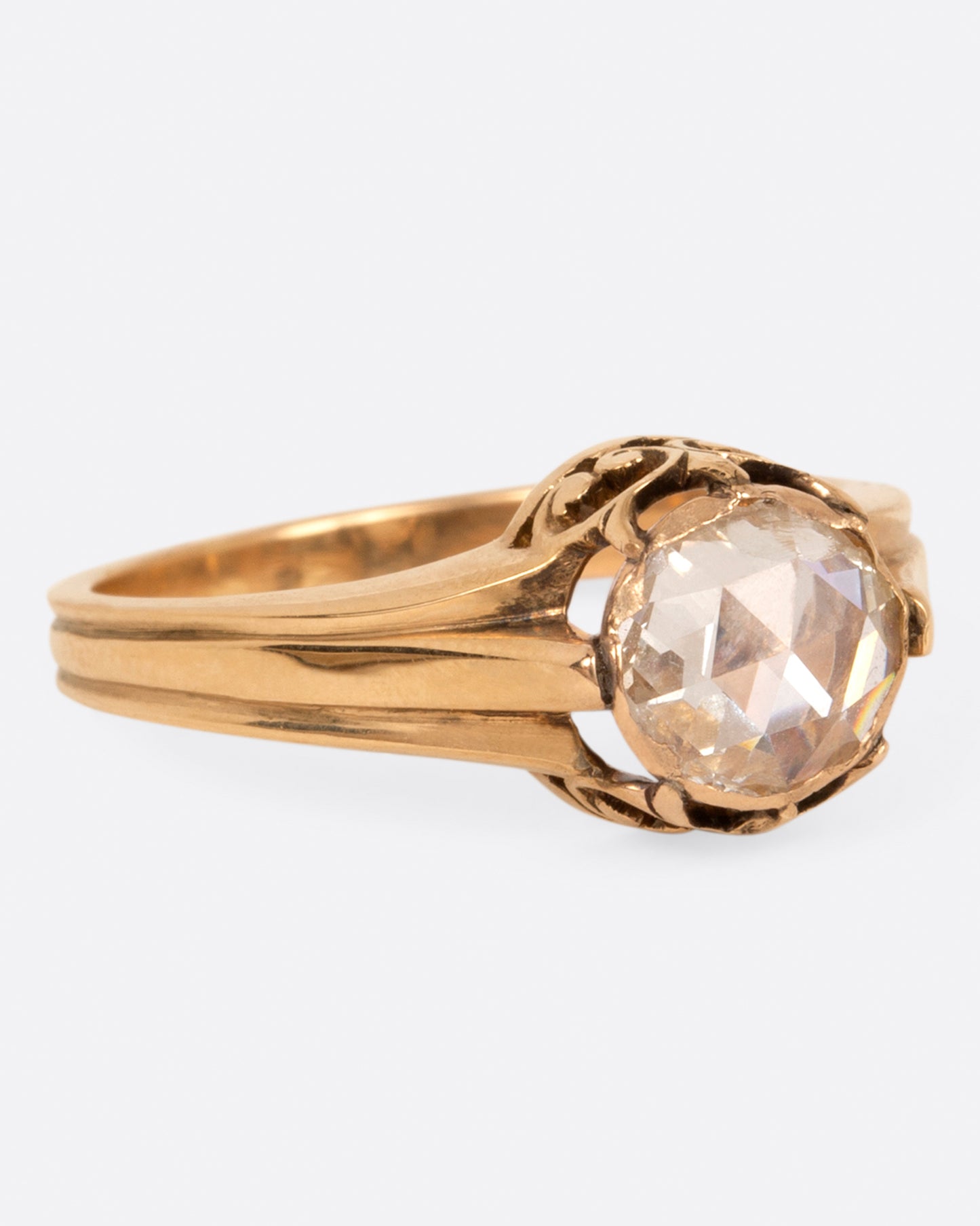 A yellow gold diamond solitaire ring with a rose cut diamond and a ribbed band, shown from the side.