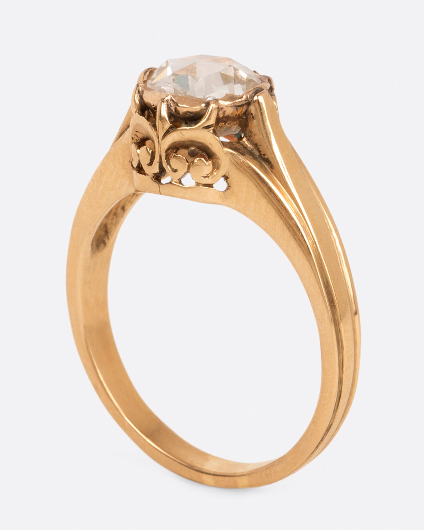 A yellow gold diamond solitaire ring with a rose cut diamond and a ribbed band, shown standing.