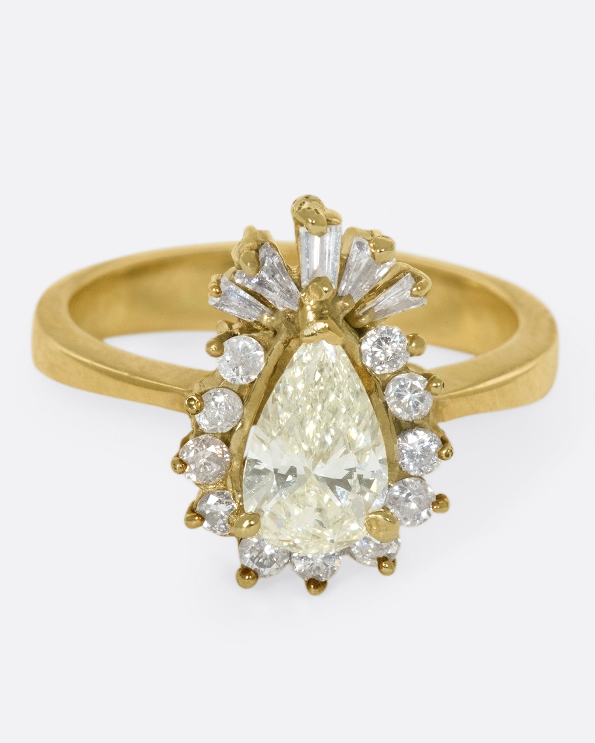 A tapered ring with a pale yellow, pear shaped diamond at its center with a round and baguette diamond halo.