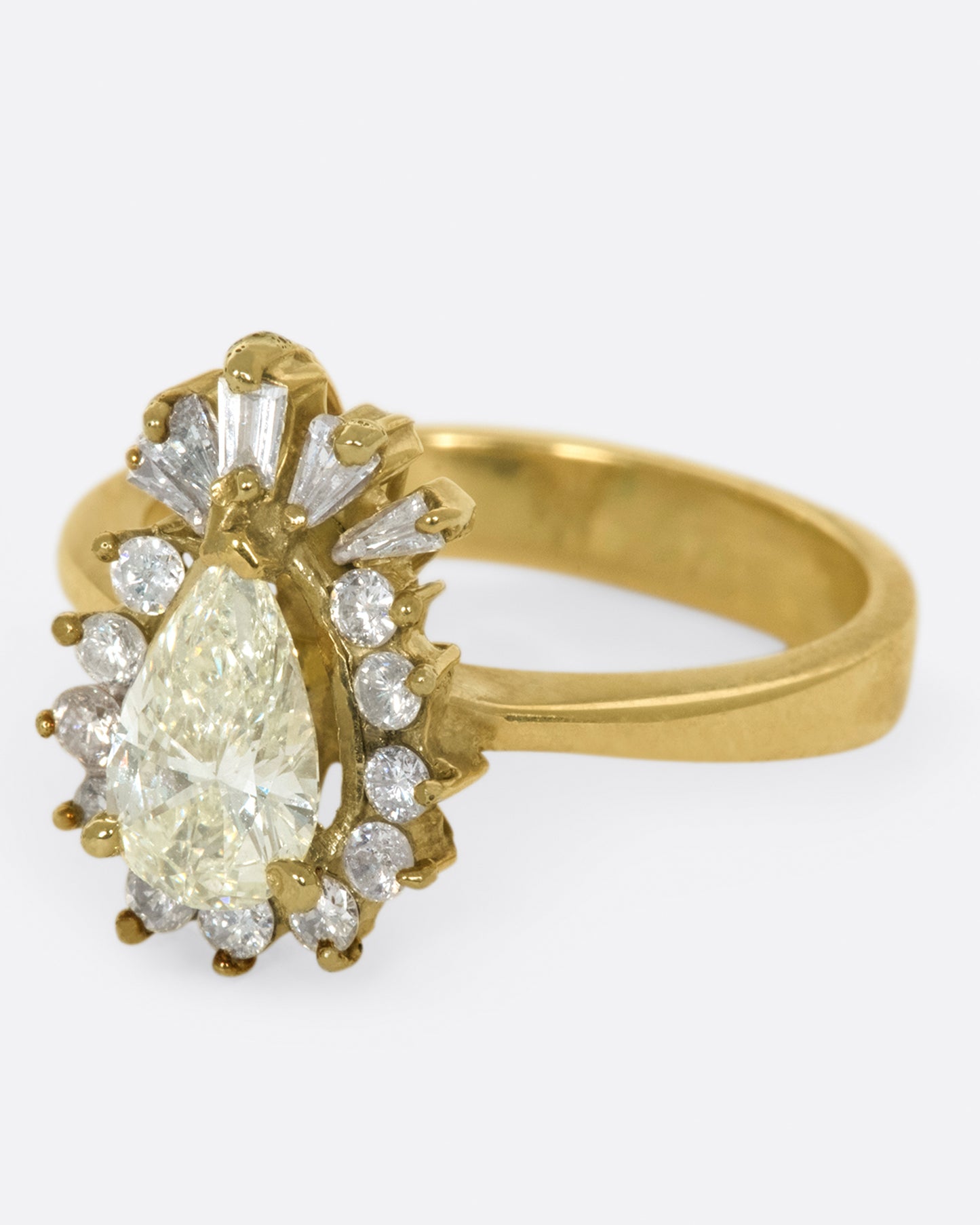 A tapered ring with a pale yellow, pear shaped diamond at its center with a round and baguette diamond halo.