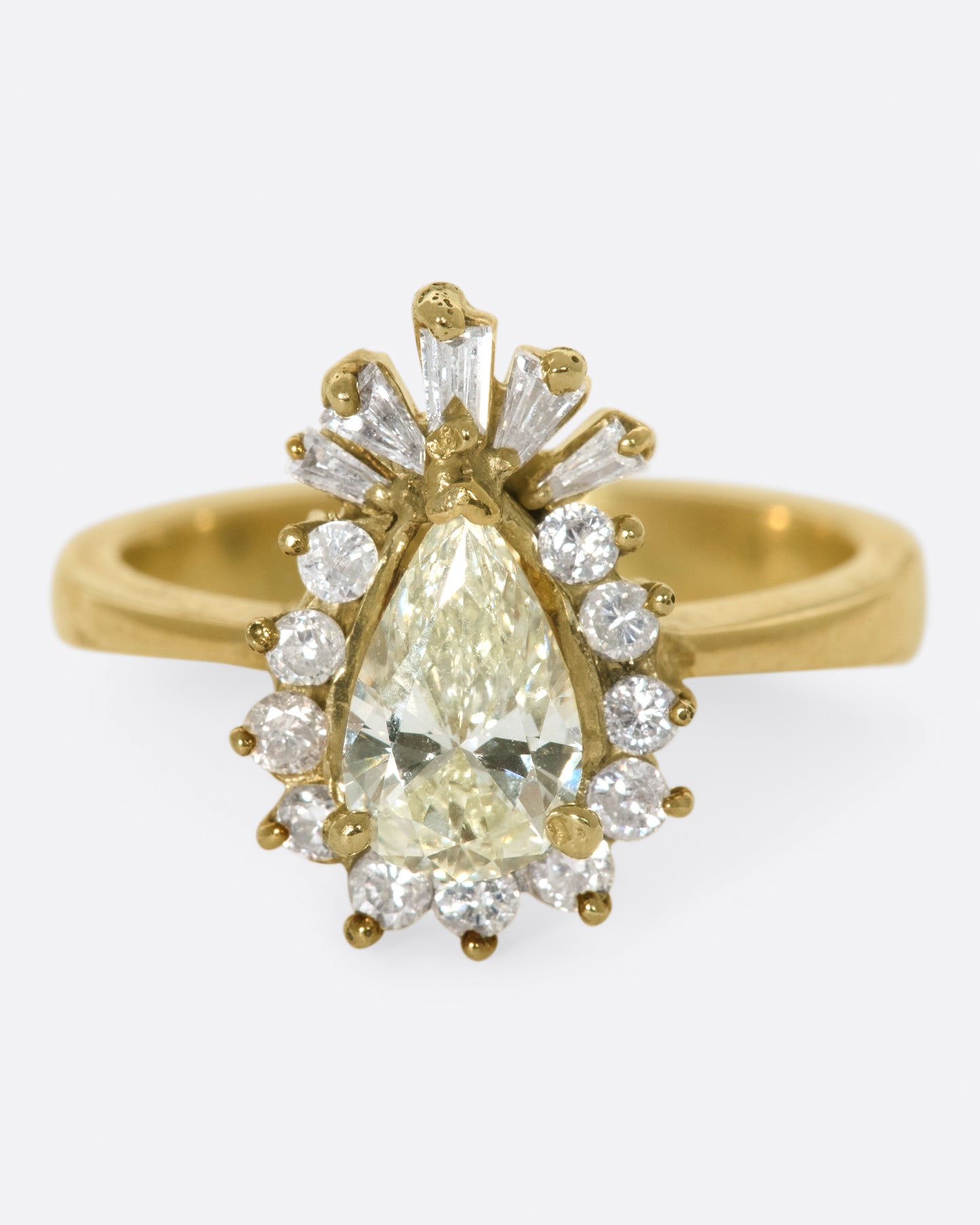 A tapered ring with a pale yellow, pear shaped diamond at its center with a round and baguette diamond halo.