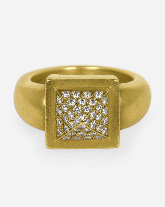 A heavy rounded gold ring with a square, pointed face covered in diamonds.