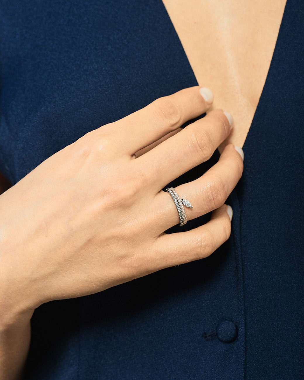 a womans hand with two rings. the bottom ring is a pave band with a dark gold setting and diamonds. the top is a pave band with a marquise diamond extending out the top.